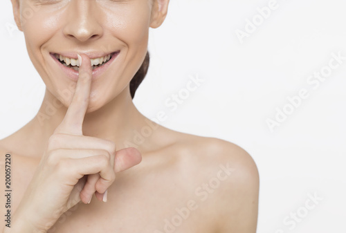 Close up Photo of a beautiful smiling female face with clean and fresh skin, the girl puts a finger to her lips.