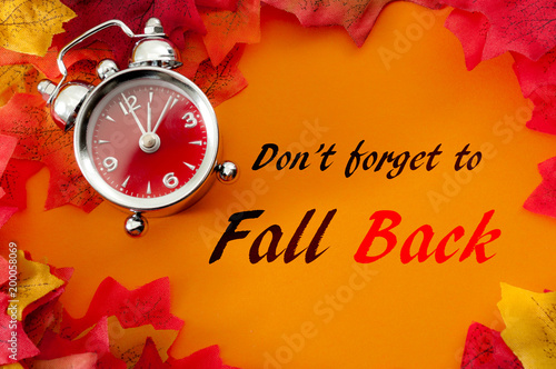 Fall back, the end of daylight savings time and turn clocks back on hour concept with a clock surrounded by dried yellow leaves with the text Don't forget to fall back