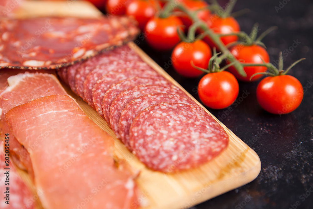 Close up of meat appetizers next to cherry tomatoes on dark wooden board Close up of meat appetizers next to cherry tomatoes on dark wooden board