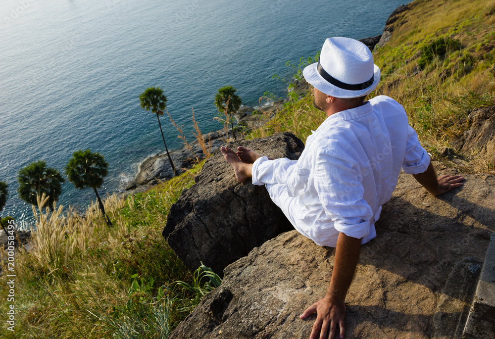 a young man sitting on a rock and looking at the sunset of Phuket