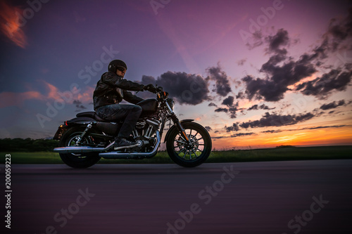 Man riding sportster motorcycle during sunset.