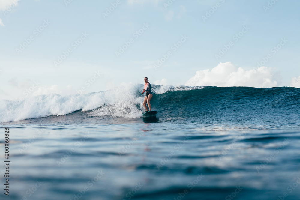 Naklejka premium young woman in wetsuit surfing on sunny day
