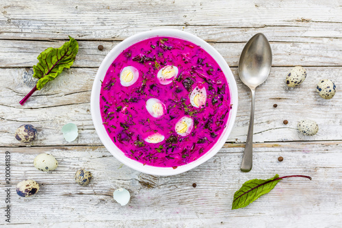 Cold soup with beetroot and quail eggs on wooden table.