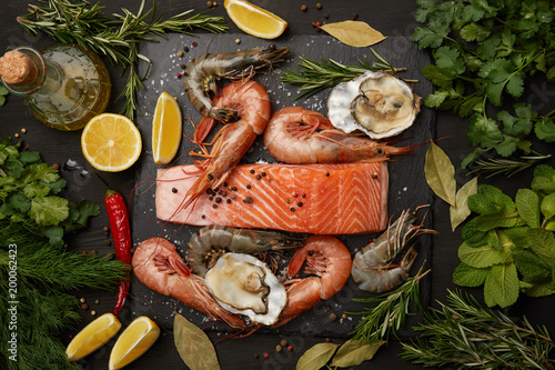 Bilde på lerret Raw salmon and assorted seafood with herbs and lemons on dark background
