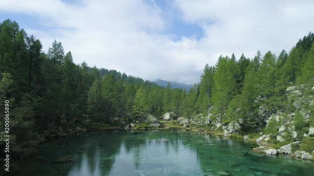 aerial forward over blue alpine lake revealing mountain forest valley in sunny summer with clouds.Europe Alps outdoors green nature scape mountains wild establisher.4k drone flight establishing shot