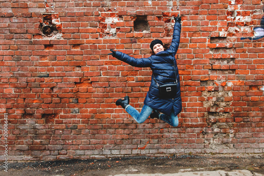 smiling girl was photographed in a jump on a brick wall background