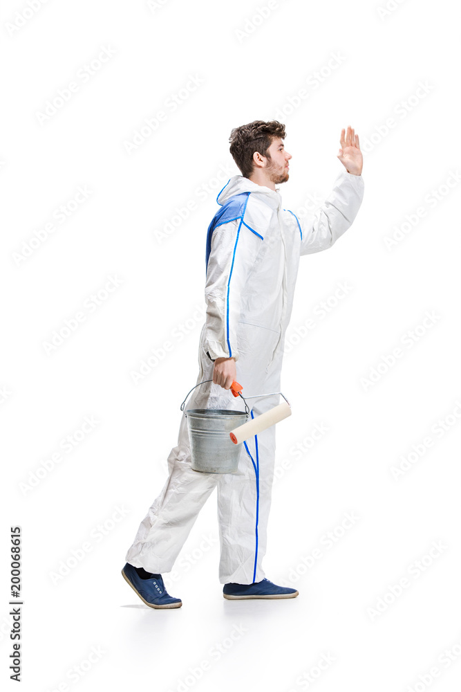 Young male decorator painting with a paint roller climbed a ladder isolated on white background.