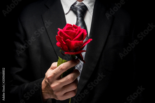 close up of man in black suit holding red rose. photo