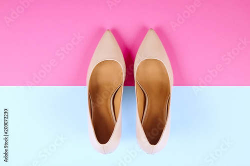 Stylish classic women's beige leather shoes with medium high heels shot from top on pink blue multi-colored paper background. Copy space, top view, flat lay. Shoe sale / clearance ad concept.
