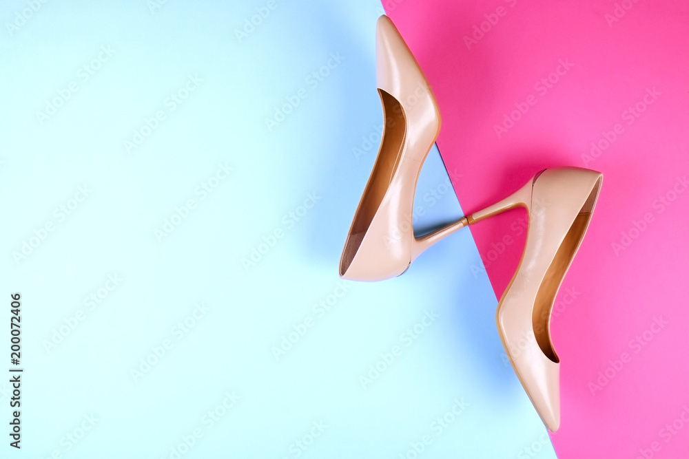 Stylish classic women's beige leather shoes with medium high heels, side shot on pink blue multi-colored paper background. Copy space, top view, flat lay. Shoe sale / clearance ad concept.