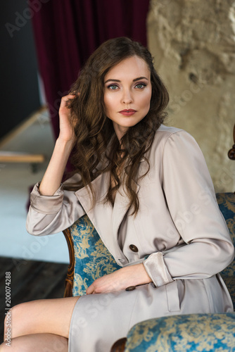 elegant woman in fashionable trench coat sitting in armchair