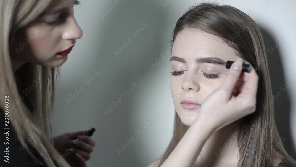 Makeup artist doing makeup for eyebrows. Young girl doing professional makeup, eyebrow shaping Makeup artist doing makeup for eyebrows. Young girl doing professional makeup, eyebrow shaping