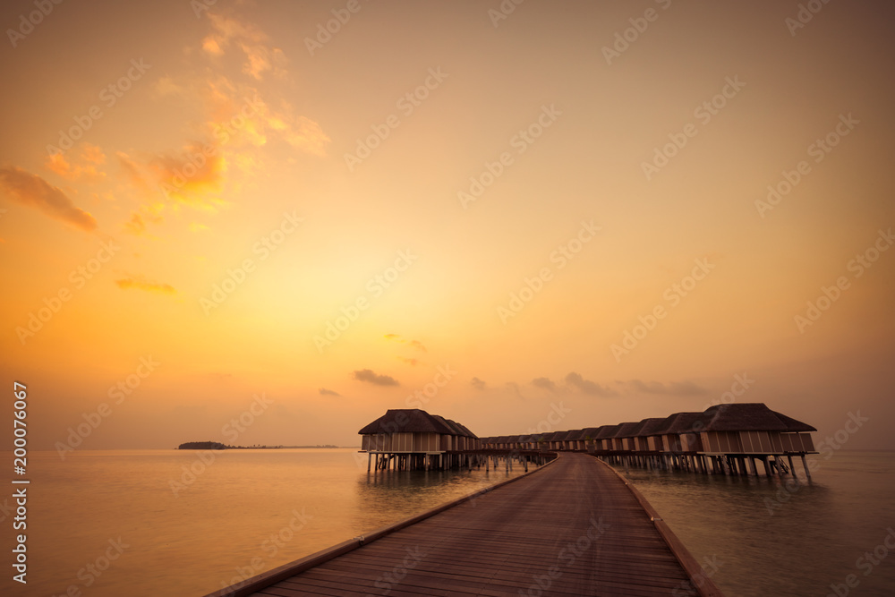 Fototapeta premium Sunset in Maldives island. Beautiful sunset sky and clouds, luxury water villas and wooden pathway - pier