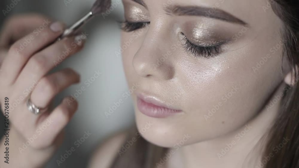 Makeup artist to apply highlighter. Young girl doing professional makeup Makeup artist to apply highlighter. Young girl doing professional makeup