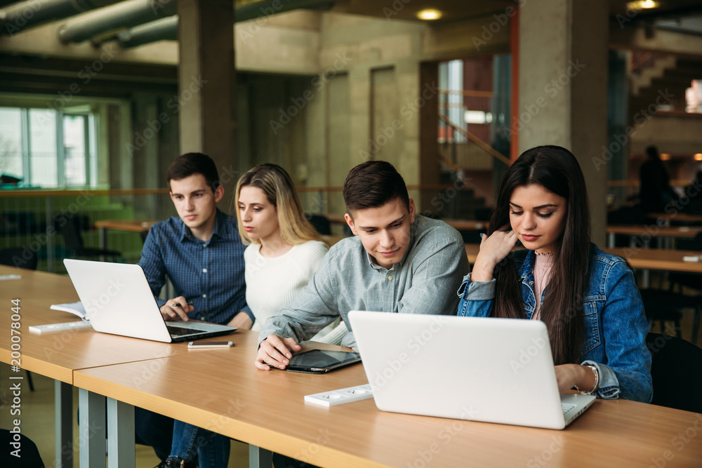 Group of college students studying in the school library, a girl and a boy are using a laptop and connecting to internet Group of college students studying in the school library, a girl and a boy are using a laptop and connecting to internet