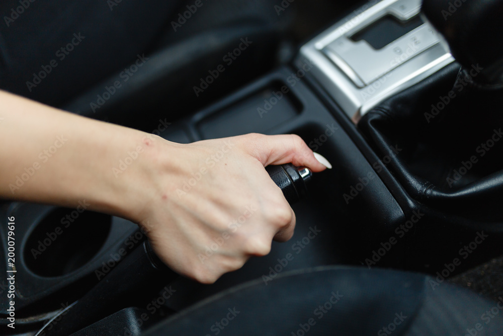 Close up of female hands holding a handbrake lever to keep the vehicle stationary. The girl puts the car in the Parking lot with the handbrake.