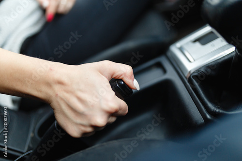Close up of female hands holding a handbrake lever to keep the vehicle stationary. The girl puts the car in the Parking lot with the handbrake.