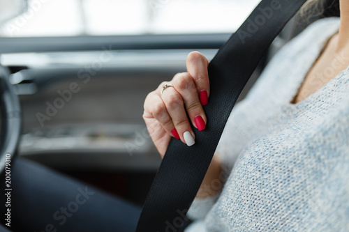 Clasp safety belt in the hands of the girl. Driver girl fasten your seat belt. Close-up Of Female's Hand Sitting Inside Car Fastening Seat Belt. Concept of safe driving while driving.