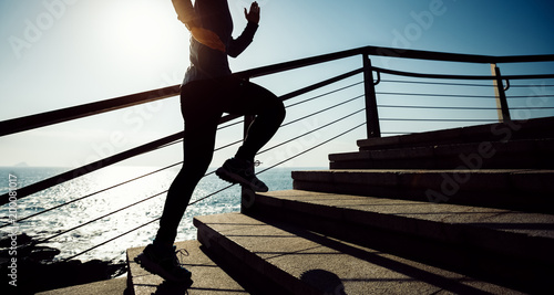 sporty female jogger running upstairs on seaside during sunrise