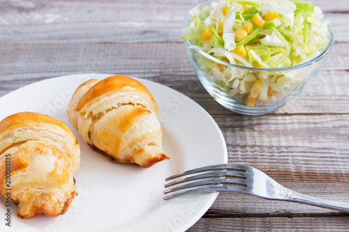 Salad and cheese salt croissant on white plate.