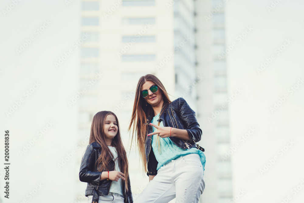 Fashion family look. Woman with child girl in family fashionable clothes having fun outdoor. Fashion young mother and child daughter wearing a sunglasses