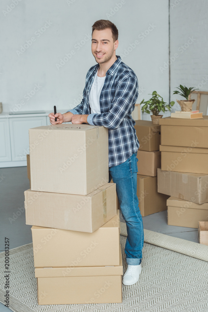 smiling man signing cardboard box for moving home, relocation concept smiling man signing cardboard box for moving home, relocation concept