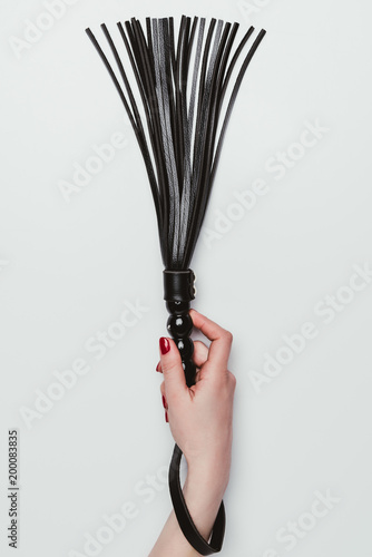 Black leather whip in female hand isolated on white photo