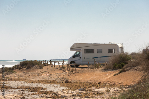 Caravan motorhome parked on the beach in front of the blue sea in a beautiful place of wild nature photo