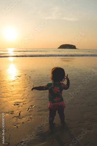 Silhouette of Happy baby girl is enjoying the golden sunset at the sand beach on the seashore of Andaman Sea