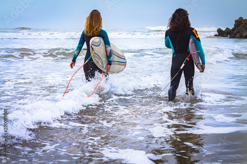 Two surfers, man and woman, close-up against the background of the Atlantic Ocean. Back view