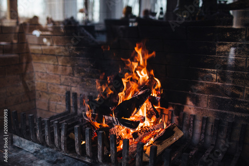 Colourful flame and burning wood at fireplace. Close up shot of bright flame which gives heat. Blazing woods and coals. Dark background image