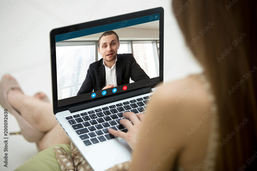 Young woman communicating with man in formal suit via video call application. Dressy couple chatting. Long distance relationship, virtual communication. Close up view over shoulder, focus on screen. Young woman communicating with man in formal suit via video call application. Dressy couple chatting. Long distance relationship, virtual communication. Close up view over shoulder, focus on screen.