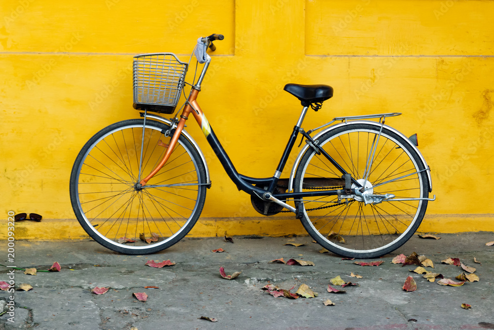 Old bicycle on a background of bright painted yellow wall and autumn leaves on a street. Old bicycle on a background of bright painted yellow wall and autumn leaves on a street.