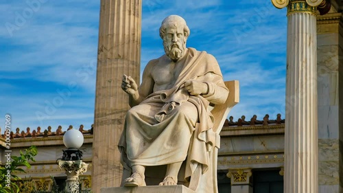 Statue of the great Greek philosopher Plato on a marble chair, background of sky and marble columns.