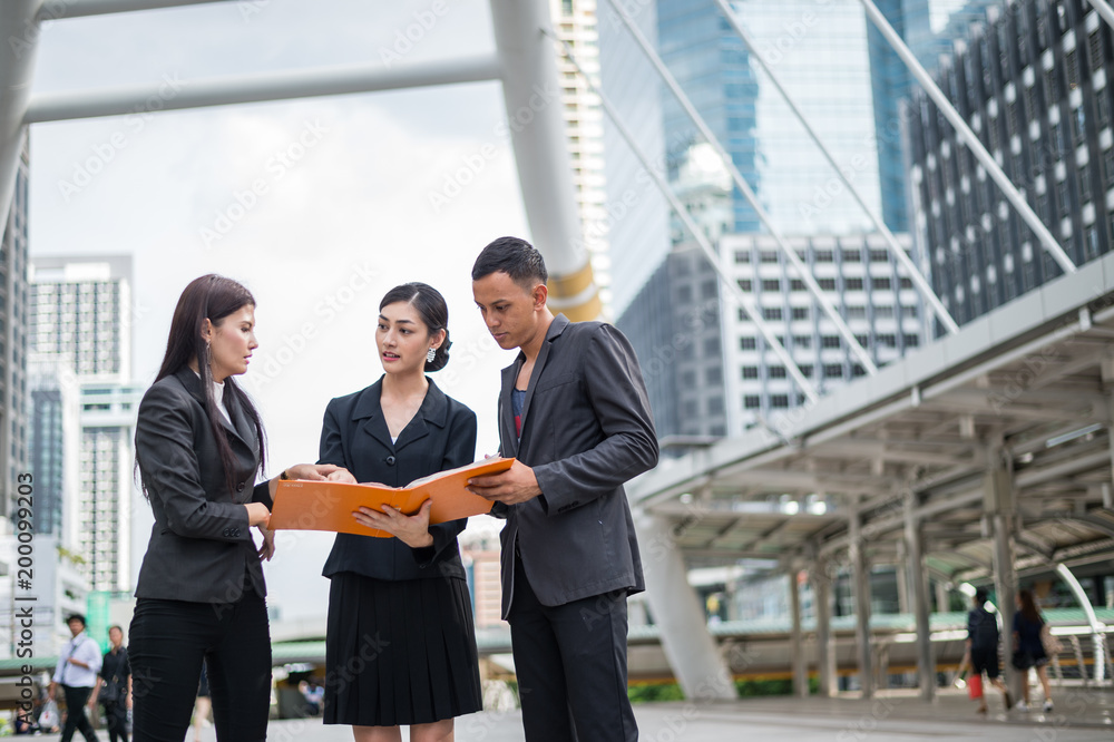 Asian business woman standing and holding financial document on hand, she talking about business future with businessman and team.