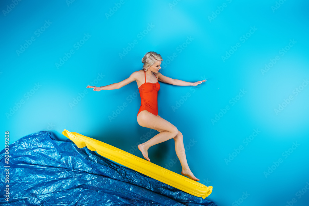 girl in swimsuit standing on inflatable mattress on blue, summer vacation concept