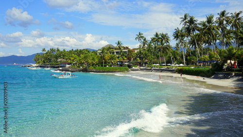 malerischer Urlaubsstrand in Candidasa in Bali mit Meer, Wellen und grünen Palmen