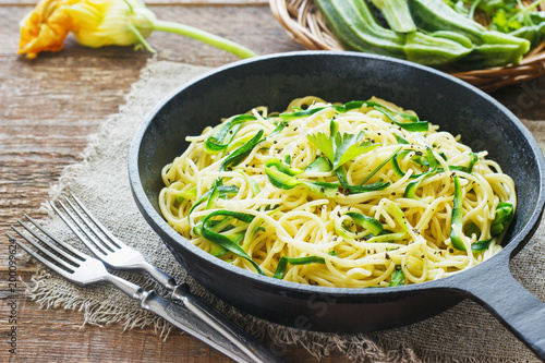 Pasta with zucchini on dark wooden background in a cast-iron frying pan . Spaghetti from organic wholegrain flour