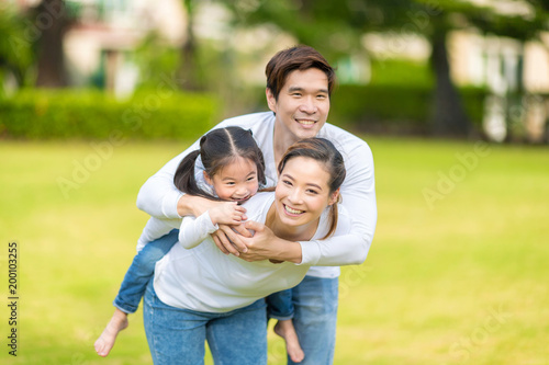 Cute Asian girl on neck parents big happy laughing and run around together.Happy family piggybacking adorable little daughter is smiling. selective focus at girl eye.