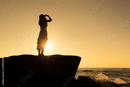 Silhouette of Asian beautiful lady wear white dress is stand posing on rock cliff.