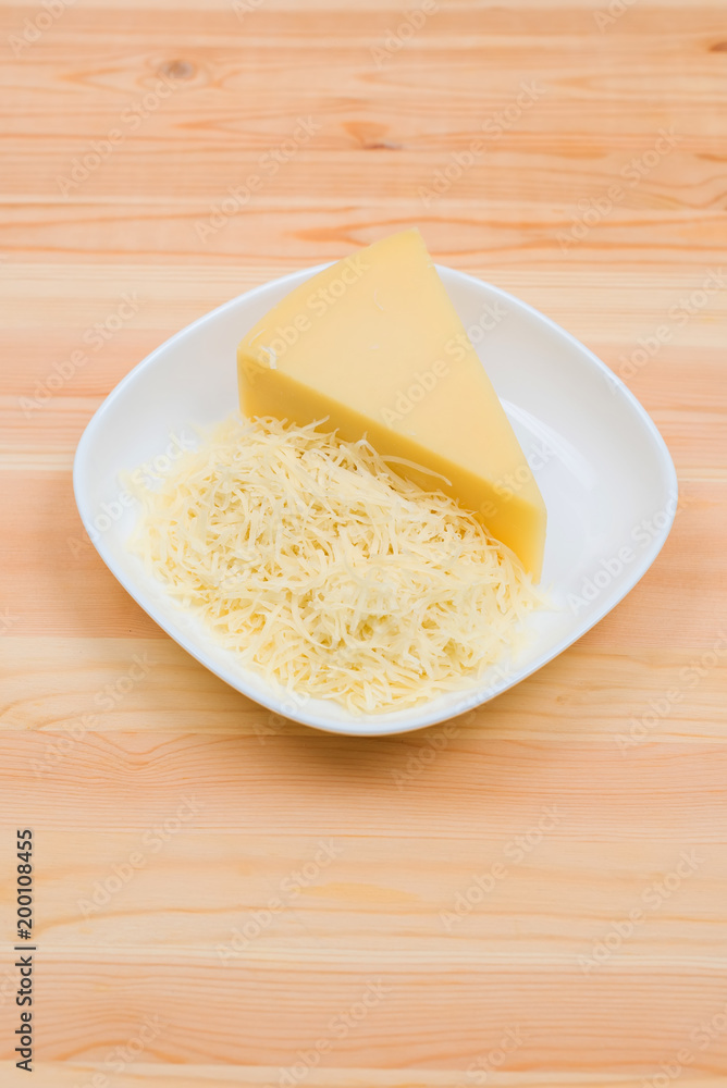 Close-up on a wooden table in a plate is Parmesan cheese in grated and brick form. The concept of solid dairy products Close-up on a wooden table in a plate is Parmesan cheese in grated and brick form. The concept of solid dairy products