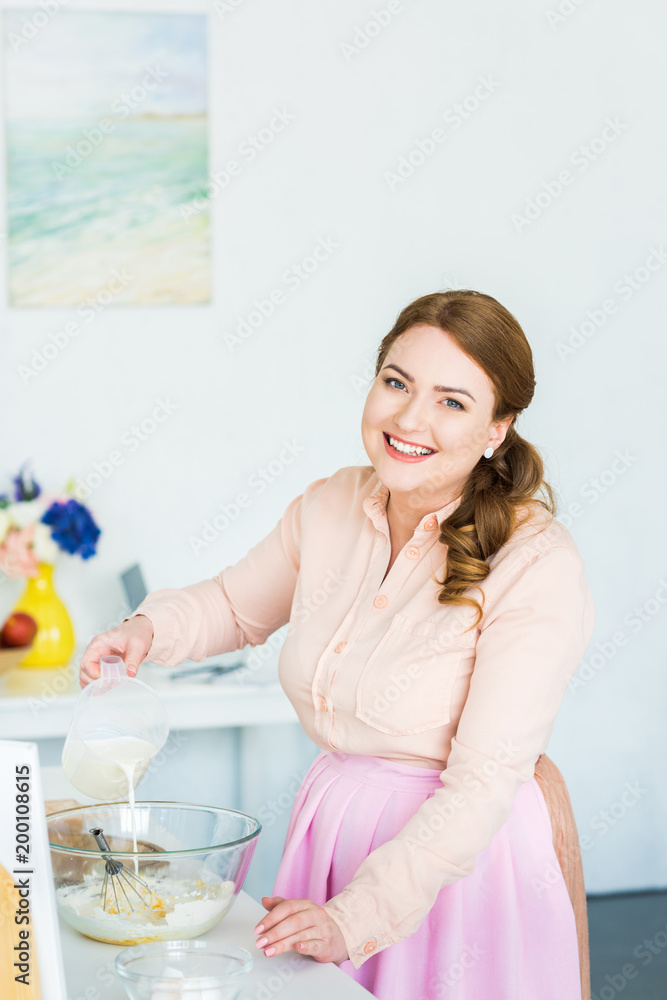 smiling beautiful woman pouring milk into bowl with flour at kitchen smiling beautiful woman pouring milk into bowl with flour at kitchen