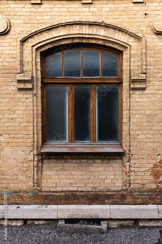 Vintage arched window in the wall of yellow brick. Black glass in a maroon dark red wooden frame. The concept of antique vintage architecture in building elements. © yanik88