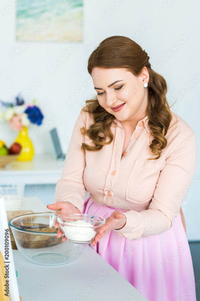 © LIGHTFIELD STUDIOS - happy beautiful woman holding bowl with flour in kitchen