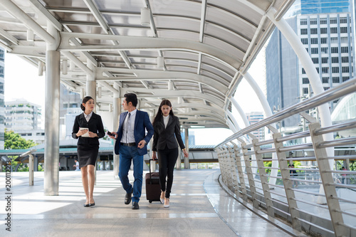 businessman and businesswoman walk together and talk about business with mobile and luggage on the public street, business travel