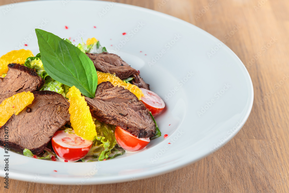  slices of boiled beef with lettuce, cherry tomatoes and orange pulp on a plate stand on an oak table