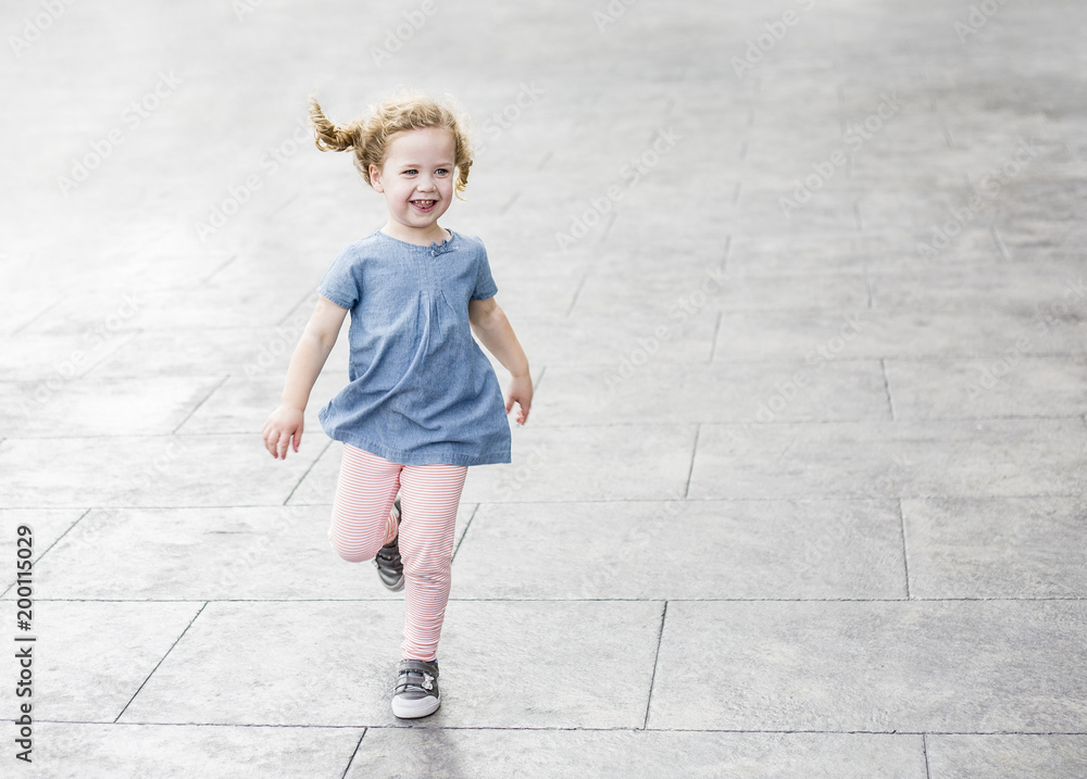 Emotional portrait of a happy energetic little girl with blond curly hair laughing as she runs around outdoors on a paved walk way. Carefree, Joy, fun and Happiness concept photo Emotional portrait of a happy energetic little girl with blond curly hair laughing as she runs around outdoors on a paved walk way. Carefree, Joy, fun and Happiness concept photo