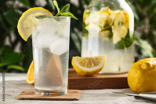 citrus mint lemonade with ice cubes in glass Cup next to vintage carafe. Summer drink Limoncello