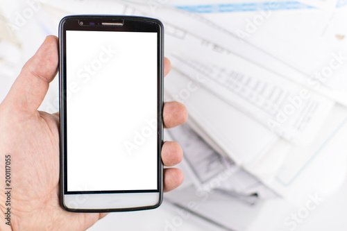 A man's hand holds a mobile phone against a background of scattered documents. mock-up.