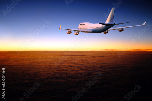 Airplane flying over layer of clouds at dawn.